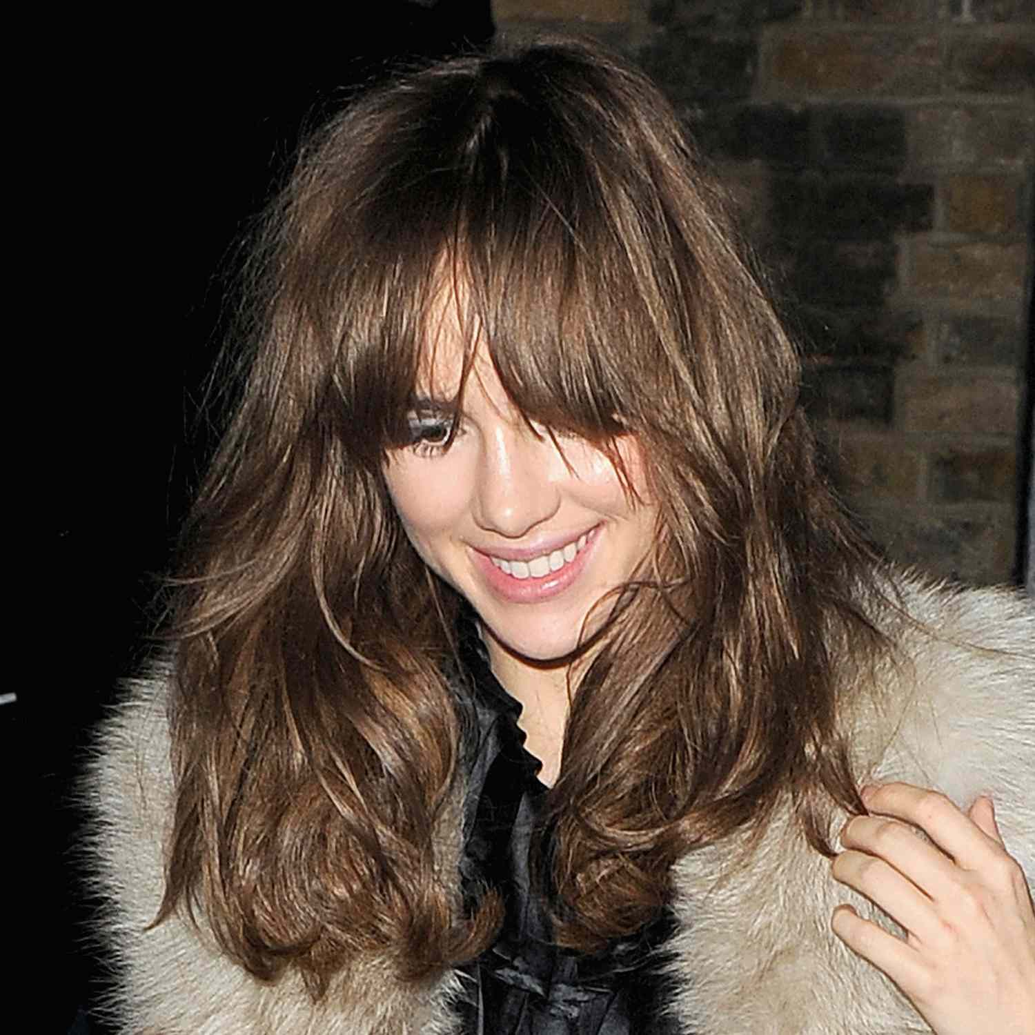 Suki Waterhouse attends a birthday party with long french bangs and full bouncy hair over a fur coat